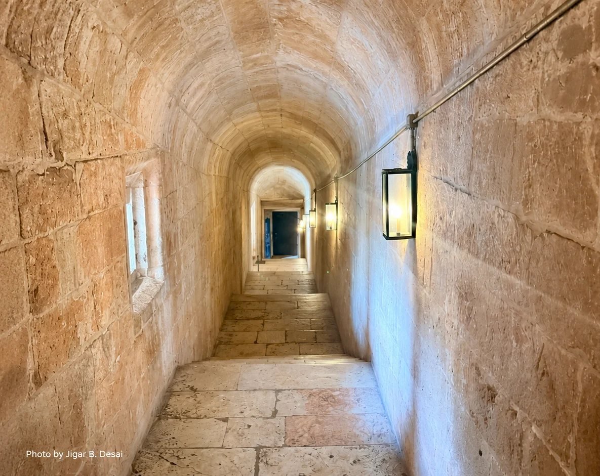 Lantern-lit vaulted stone corridor at the Jerónimos Monastery, narrowing toward a distant doorway